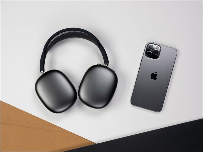 Los AirPods Max y el iPhone negros están apoyados contra la superficie de una mesa.