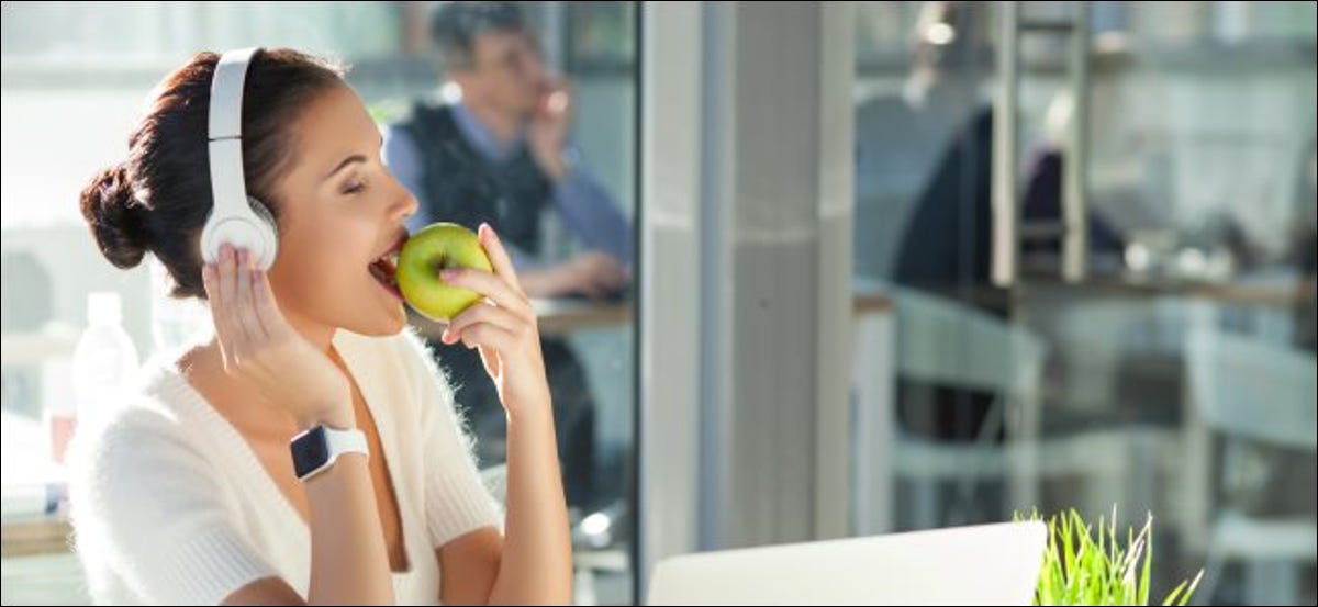 Une femme portant des écouteurs tout en portant une Apple Watch et en mangeant une Apple.