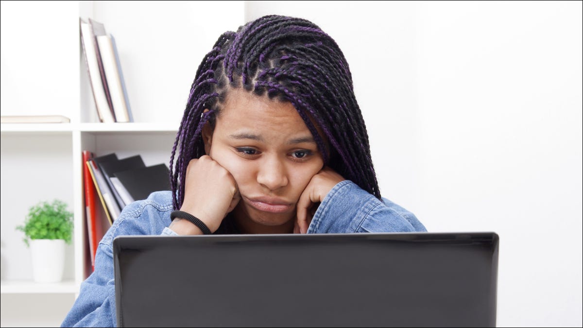 Mujer mirando la pantalla de un portátil con mirada cansada en su rostro.