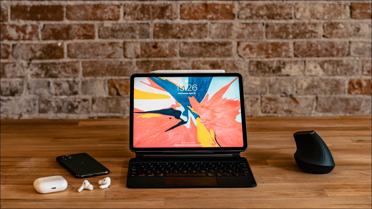 iPad sobre una mesa con un teclado Magic, iPhone, AirPods y mouse de computadora