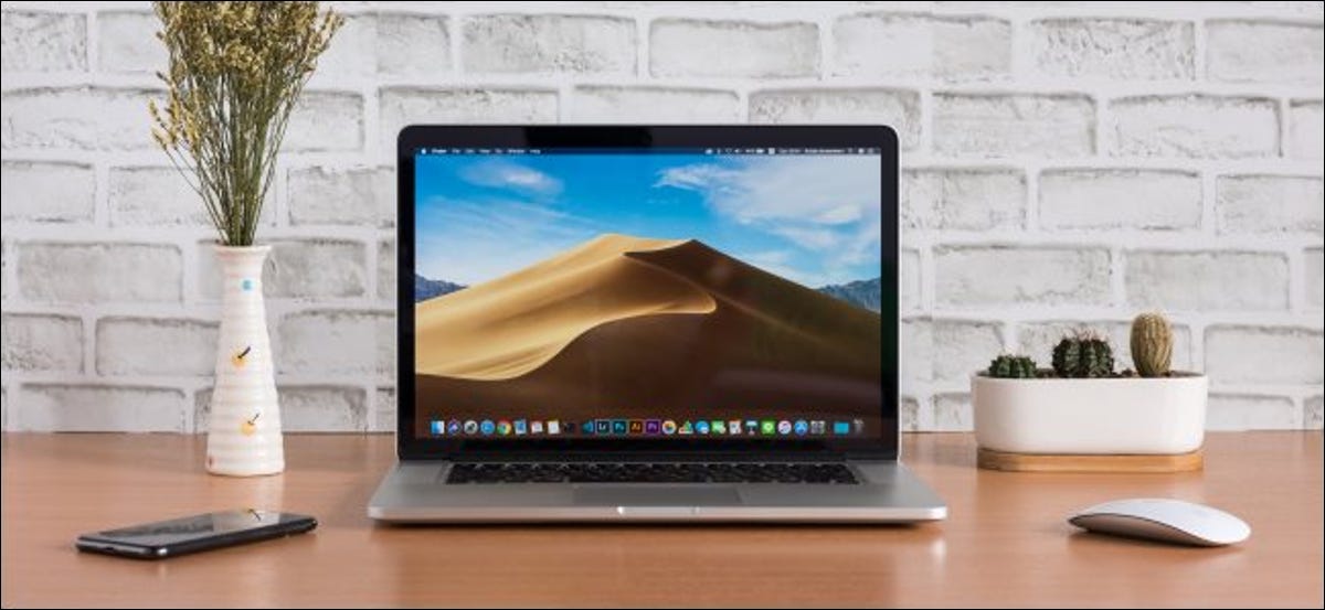 Una MacBook abierta sentada en un escritorio junto a un mouse y un teléfono inteligente.