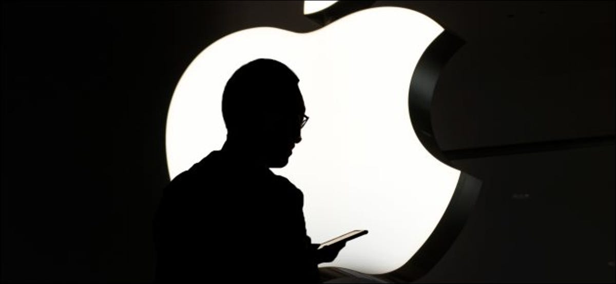 Una silueta de una persona que usa un iPhone frente a un logotipo de Apple.