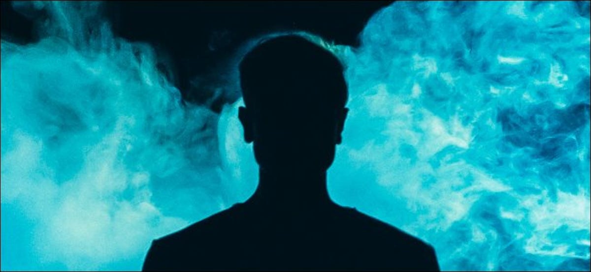 Una silueta de un individuo frente a humo azul sobre un fondo oscuro.